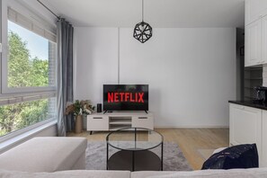 A modern living room with a flat-screen TV, a glass coffee table, and a view of the outdoors. - Apartment near River Walks (Warszawa 2)