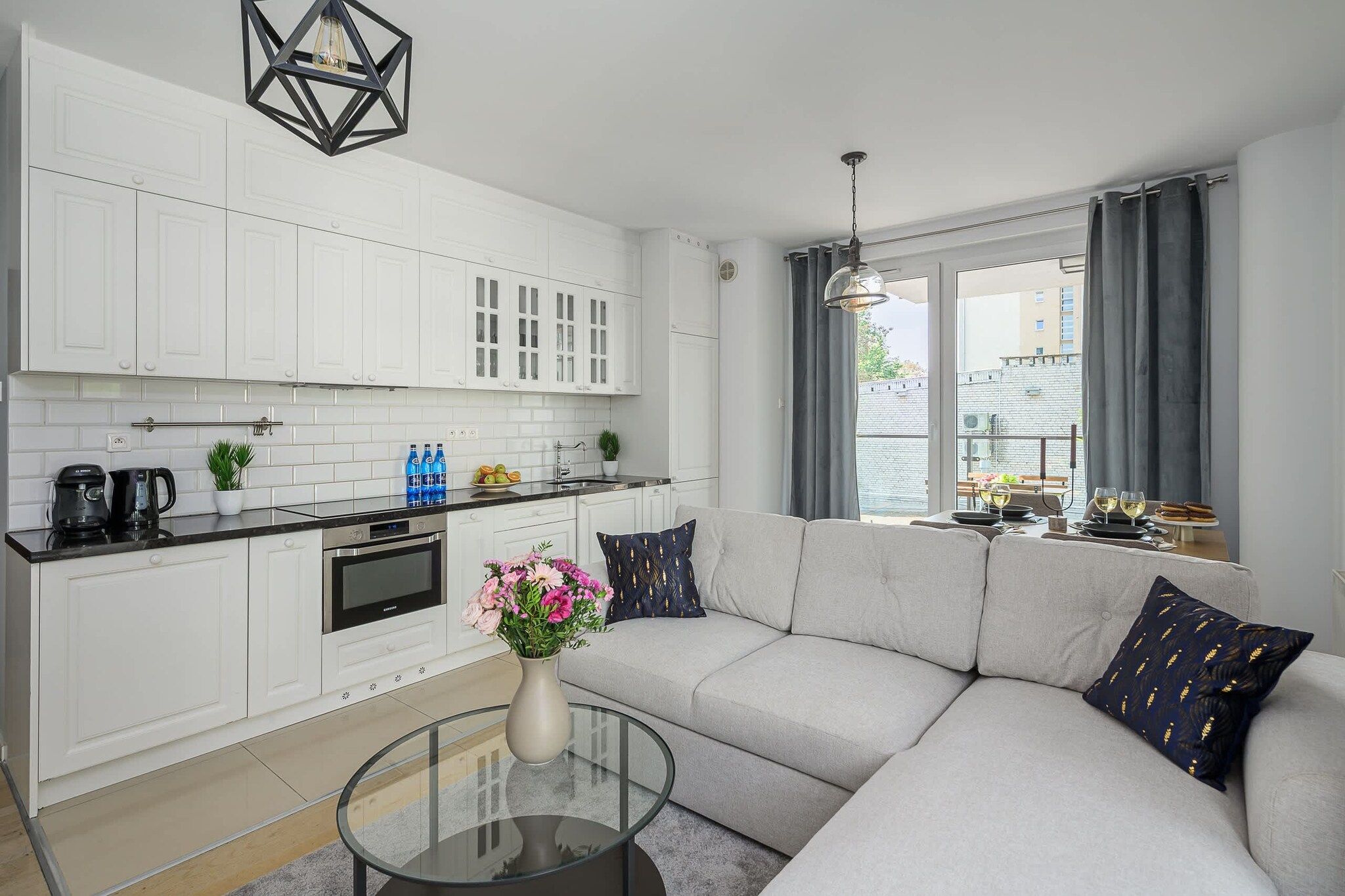 A modern kitchen with white cabinets, a black countertop, and a dining area with a glass table and sofa.