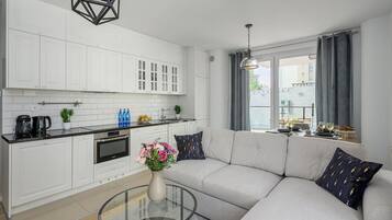 A modern kitchen with white cabinets, a black countertop, and a dining area with a glass table and sofa.