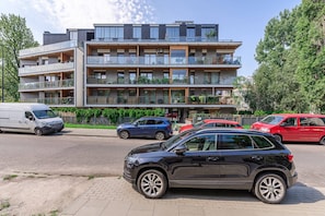 Een meerlaags woongebouw met balkons, een verharde oprit en geparkeerde auto's.