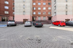 Un estacionamiento con cinco coches aparcados frente a un edificio de varios pisos con fachada roja y color crema.