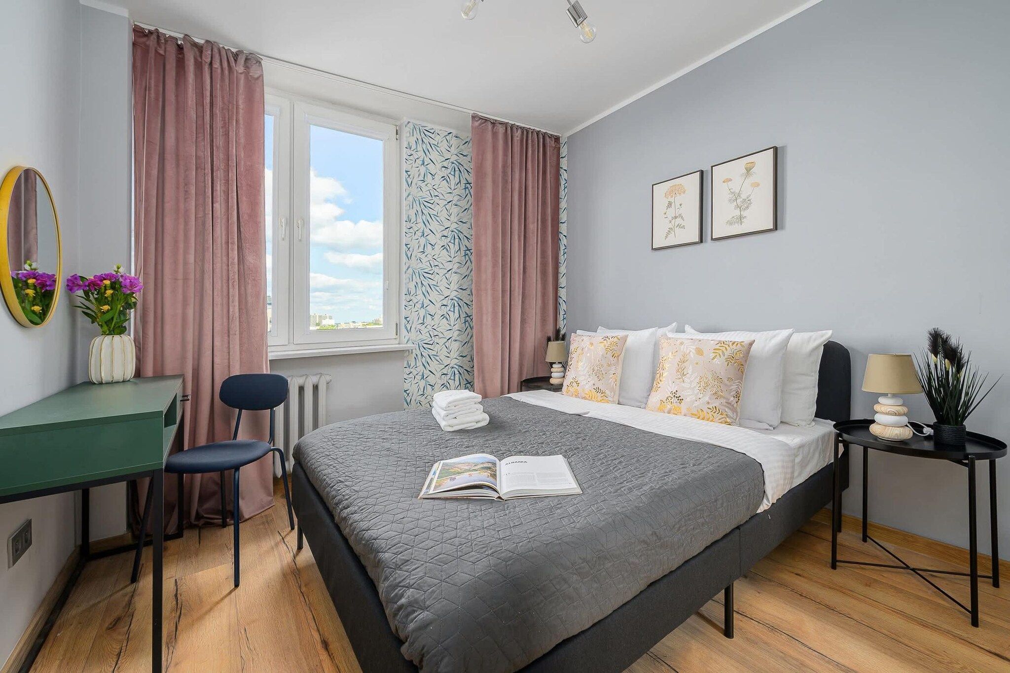 Quarto com cama, escrivaninha, cadeira, janela com cortinas e parede com quadros.
