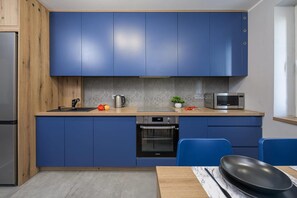 Una cocina moderna con armarios azules, un refrigerador de acero inoxidable, un microondas y un horno Samsung.