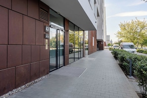 A modern building with a glass entrance, a paved walkway, and a parking area with vehicles. - Retreat by Park Skaryszewski (Warszawa)