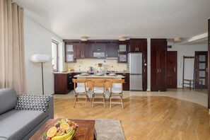 Une cuisine moderne avec des meubles de couleur bois foncé, un réfrigérateur en acier inoxydable et un coin repas doté de chaises en bois.