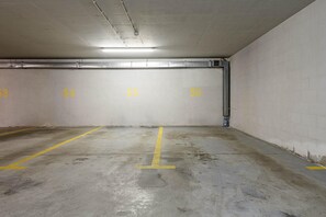 An empty parking garage with concrete walls and floors, marked parking spaces 53 to 56, and overhead fluorescent lighting. - Urban Oasis with Balcony near Zoo (Warszawa)