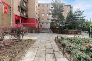 Ein mehrstöckiges Wohngebäude mit roter Fassade, einer Treppe zum Eingang und einem Garten mit blühenden Pflanzen.