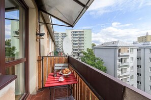 Ein Balkon mit Tisch für zwei Personen, ein Vogel auf der Mauer und Blick auf Wohnhäuser.