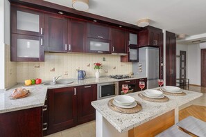 A modern kitchen with dark wood cabinets, a central island with seating, a built-in microwave, and a stainless steel refrigerator. - Urban Oasis with Balcony near Zoo (Warszawa)