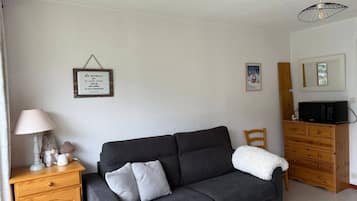 Een gezellige woonkamer met een donkergrijze bank, een houten kast, een lamp en een ingelijste quote aan de muur.
