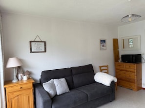 A cozy living room with a dark grey sofa, a wooden cabinet, a lamp, and a framed quote on the wall.