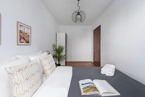 A modern bedroom with a bed, a bedside table, a potted plant, and a door. - Riverside Flat with Balcony (Warszawa)