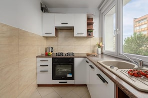 Cocina moderna con armarios blancos, horno empotrado, estufa a gas y ventana con vista a edificios.