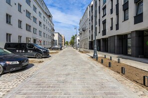 Un trottoir pavé bordé de bâtiments modernes, avec des voitures garées le long.