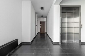 A modern hallway with a dark tiled floor, a wooden door at the end, and a metallic elevator on the right. - Large Flat with Courtyard (Warszawa)