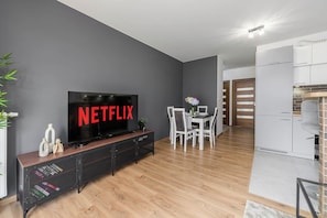 A modern living room with a flat-screen TV, wooden flooring, and a dining area with white furniture. - Central Apartment near Museums (Warszawa)