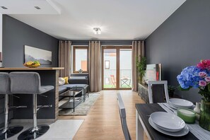 A modern living room with a sofa, coffee table, and a dining area with a TV and flowers. - Central Apartment near Museums (Warszawa)
