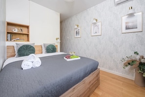 A bedroom with a bed, a bedside table with books, a wall-mounted shelf, and a potted plant. - Saska Apartment near Old Town (Warszawa)