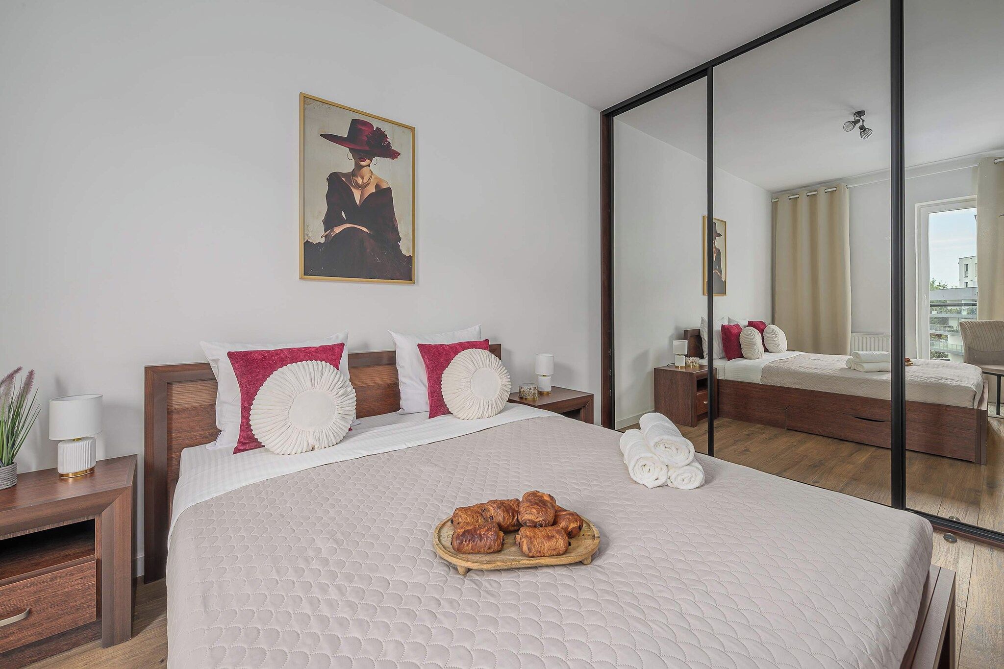 A hotel room with a large bed, a bedside table with a lamp, a mirror, and a painting on the wall.