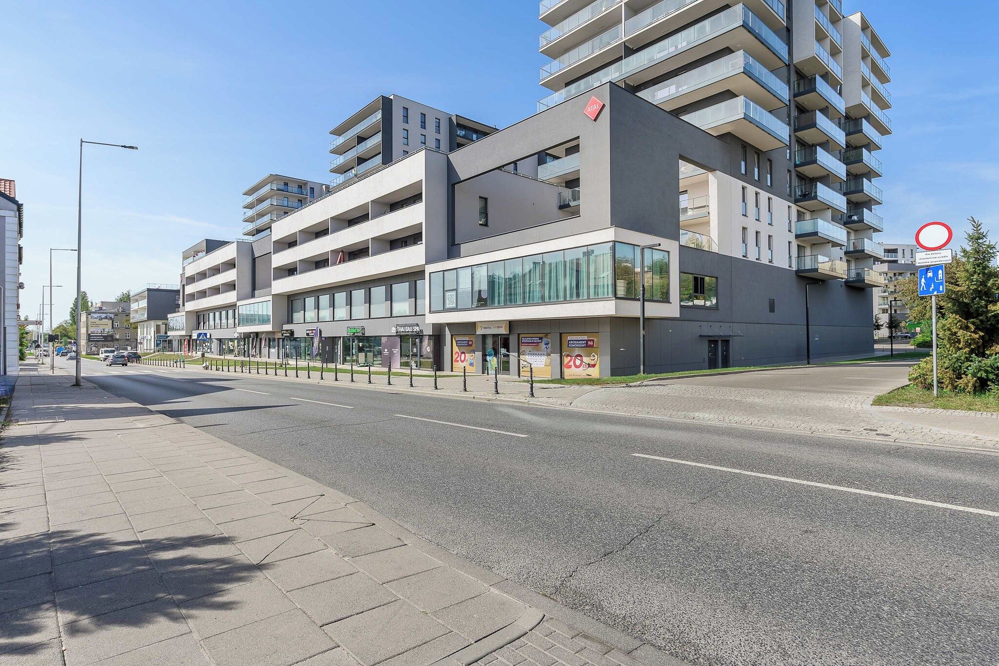 A modern multi-story building with balconies, a clear sky, and a pedestrian crossing.