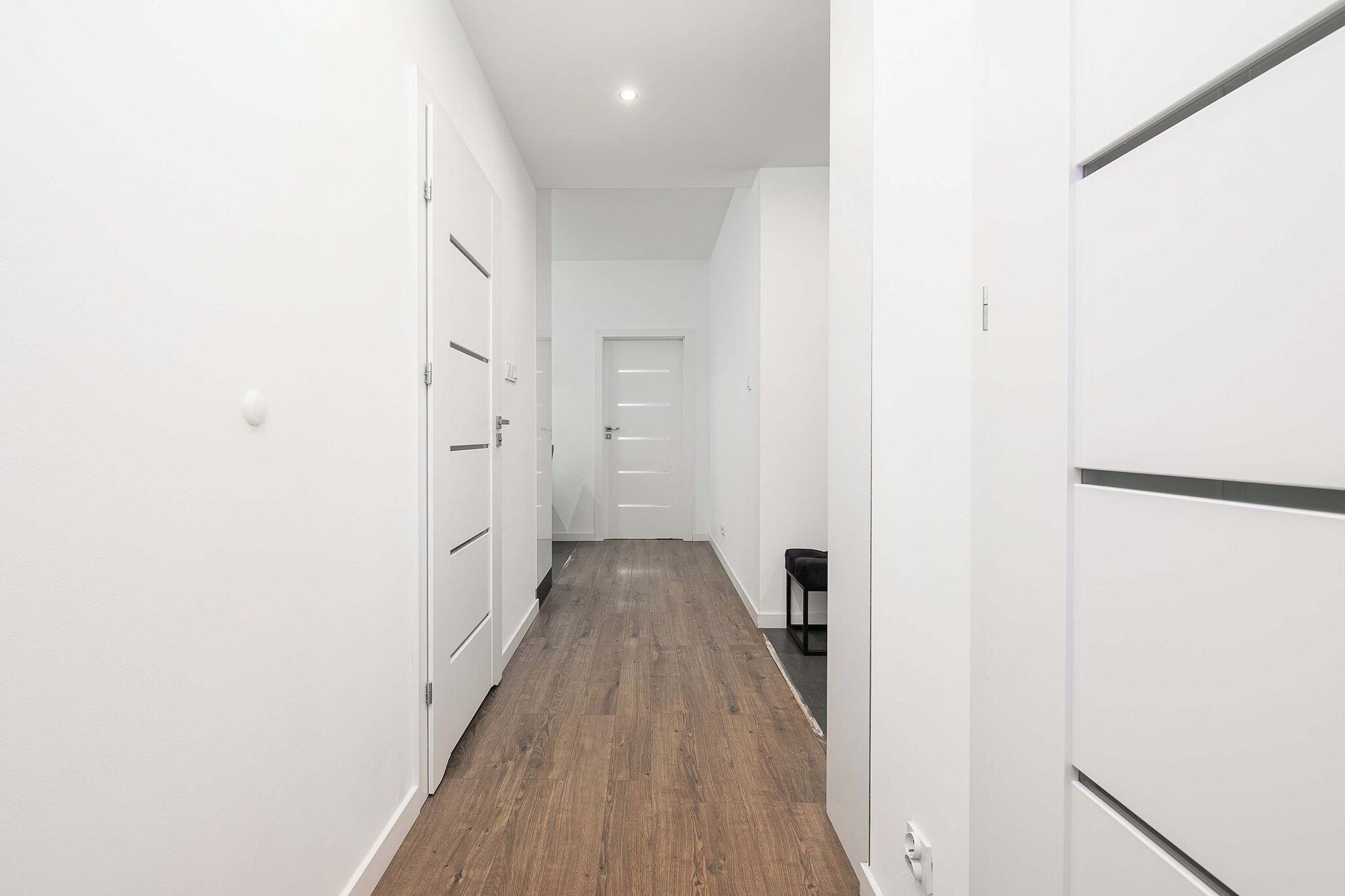 A hallway with white walls, wooden flooring, and a door at the end.