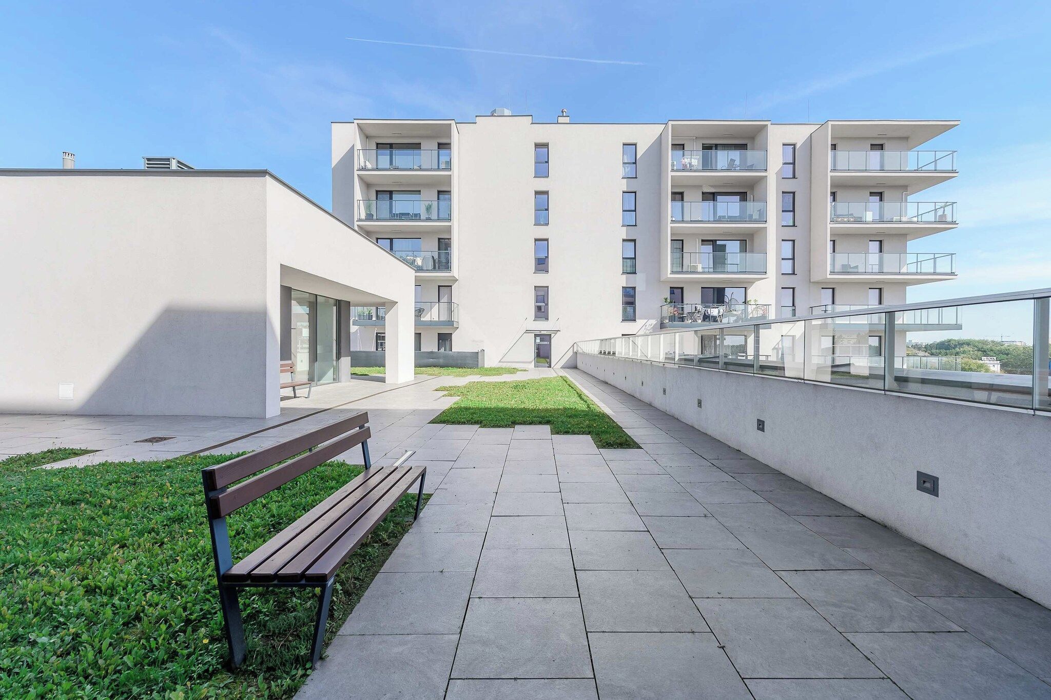 A modern apartment building with a central courtyard, a bench, and a glass railing.