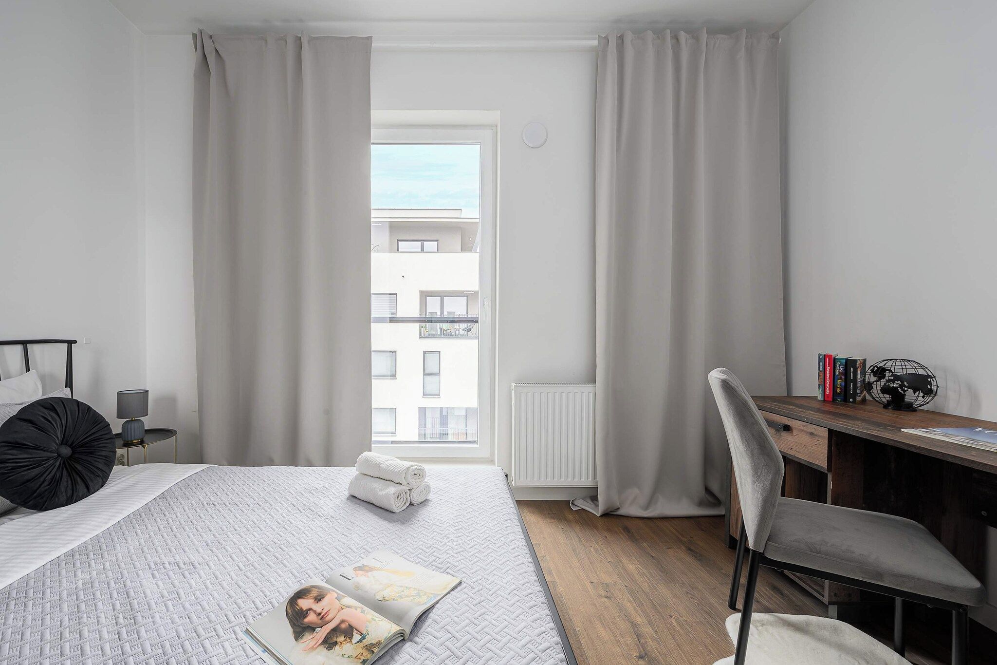 Een moderne slaapkamer met een bed, een bureau en uitzicht op een gebouw.