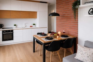 Eine moderne Küche mit weißen Schränken, einem schwarzen Backofen und einem Essbereich mit einem Holztisch für zwei Personen.