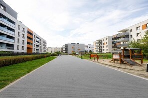 Ein modernes Wohngebiet mit mehrstöckigen Gebäuden, gepflasterten Wegen und einem kleinen Park mit Bänken.