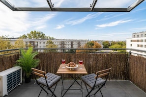 Uma varanda com mesa, duas cadeiras, uma planta e vista para edifícios.