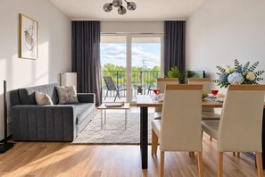 Una sala de estar moderna con un sofá gris, una mesa de comedor con sillas y vistas al exterior a través de amplias ventanas.