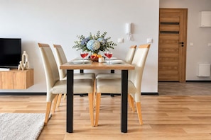Un comedor con una mesa dispuesta para cuatro personas, rodeada de sillas, un jarrón con flores y un frutero.