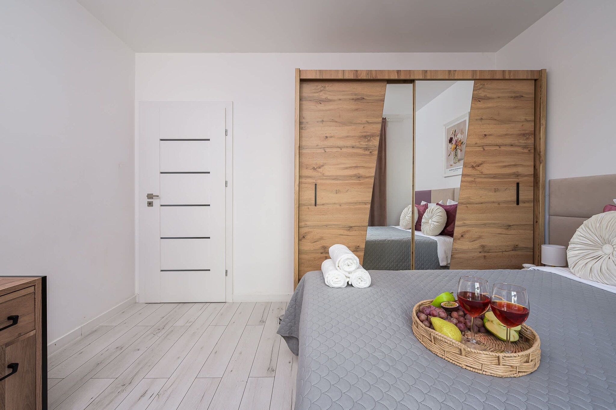 Un dormitorio con una cama, un armario de madera, una puerta blanca y un espejo fijado a la pared.