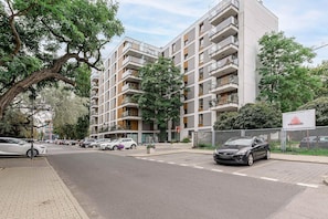 A multi-story residential building with balconies, a parking area, and a street view. - Cozy Apartment with Skyline View (Warszawa)