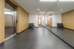 A modern hallway with a mirrored wall, a black leather bench, and a door with a metallic handle. - Cozy Apartment with Skyline View (Warszawa)