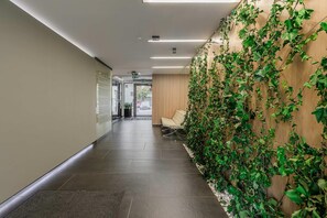 A hallway with a wall covered in green ivy, a bench, and a door leading to an outdoor area. - Cozy Apartment with Skyline View (Warszawa)