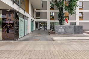 A modern building entrance with a glass facade, a flag, and a sign for 'Union Apartments.' - Cozy Apartment with Skyline View (Warszawa)