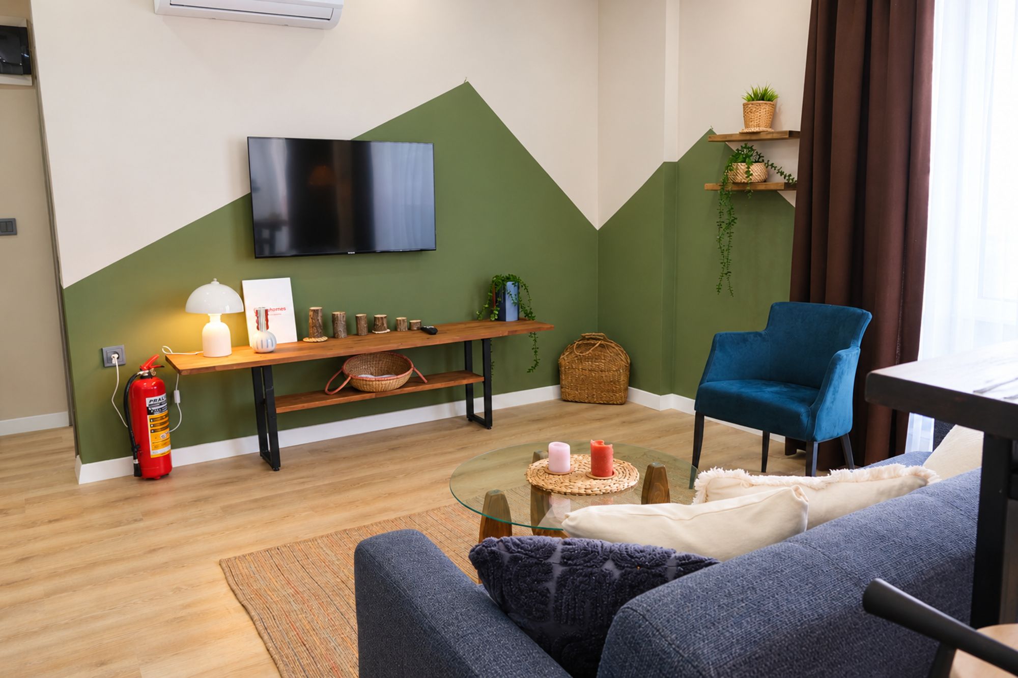 A modern living room with a flat-screen TV, a blue armchair, a sofa, a coffee table, and a fireplace.