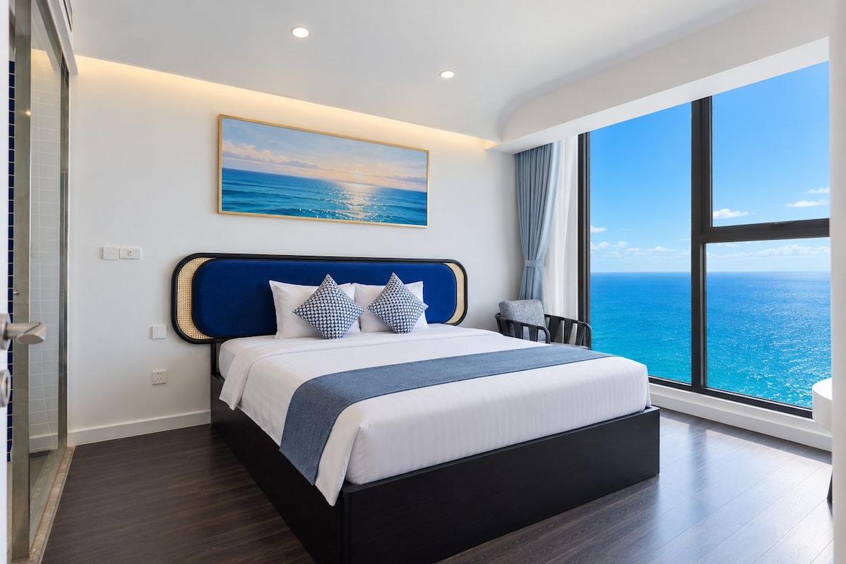 A modern hotel room with a large bed, a view of the ocean, and a painting above the bed.