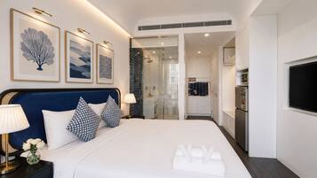 A hotel room with a bed, bedside lamps, a TV, a bathroom with a shower, and a kitchenette.