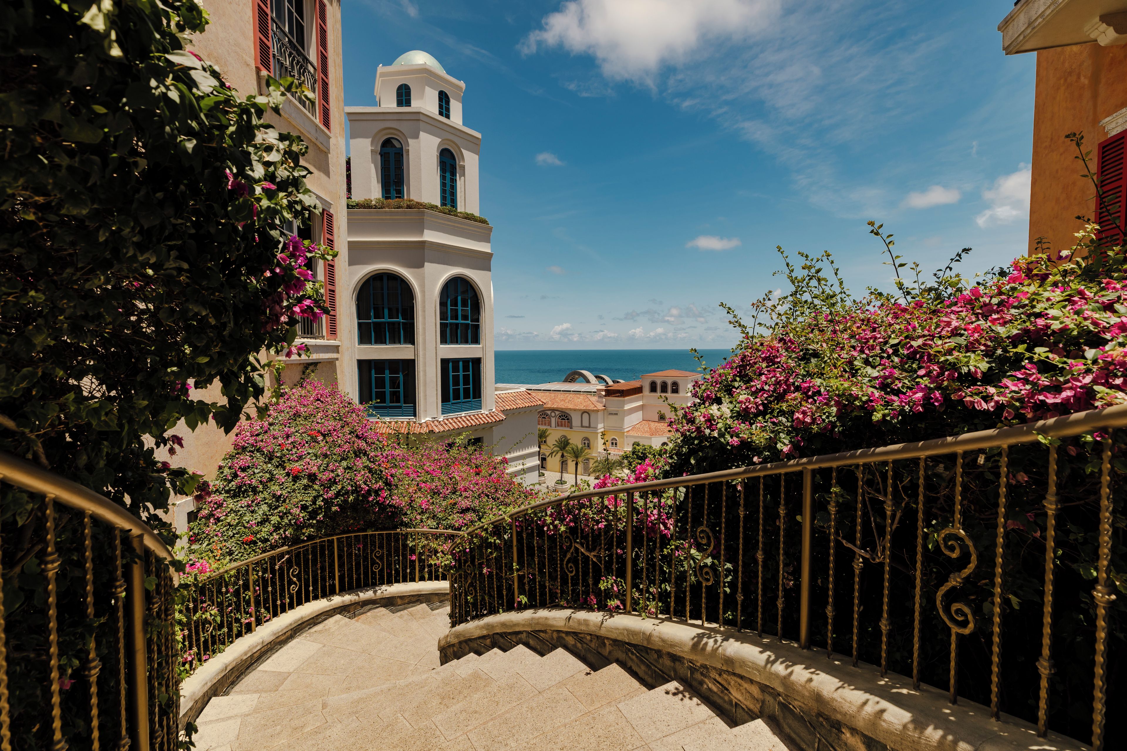 A staircase with a view of a coastal town, including a prominent white building with a tower.