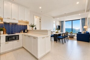 A modern kitchen with white cabinets, a blue backsplash, and a dining area with a view of the sea. - Rei Gallery Appartments Hillside (Phu Quoc)