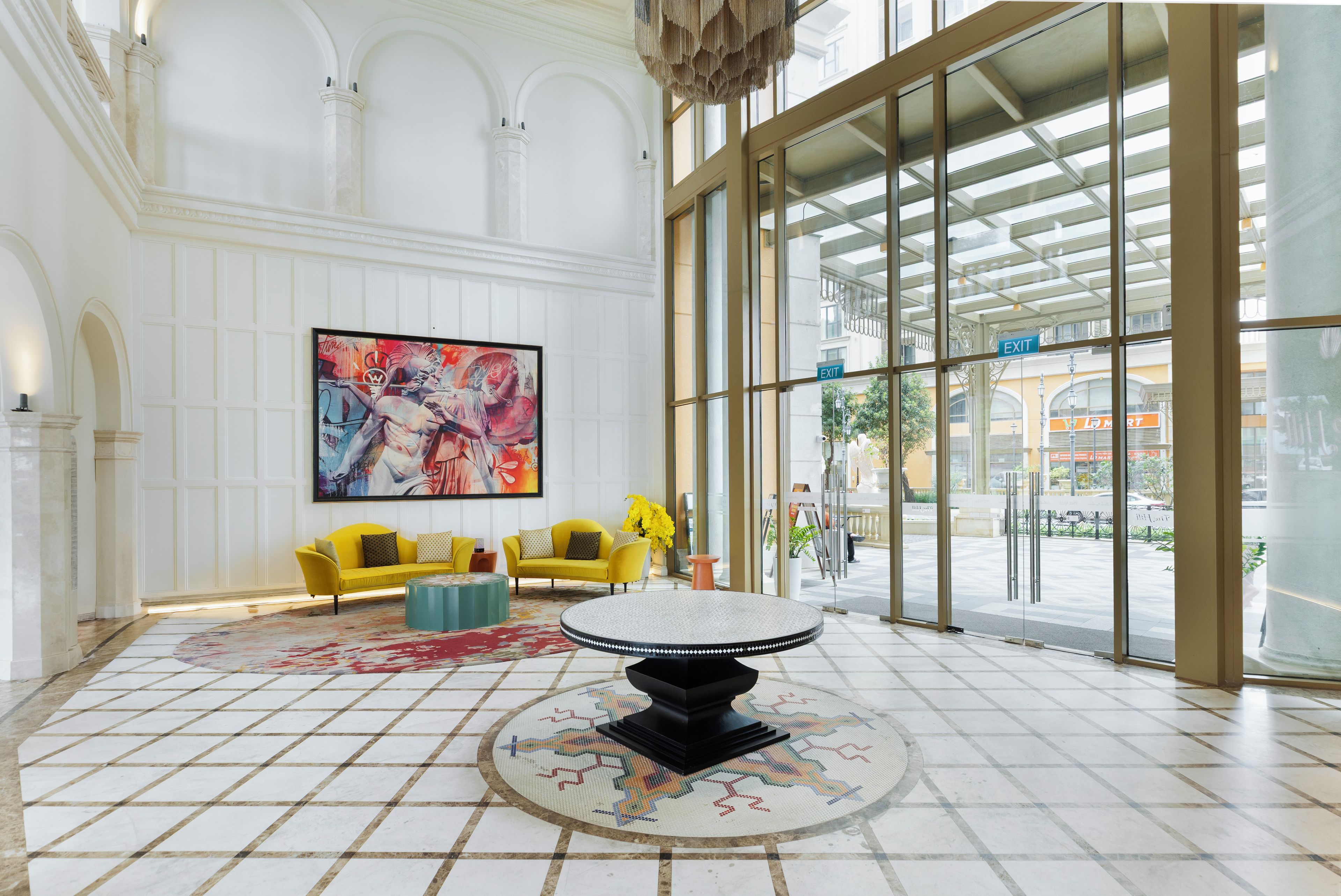 A lobby with a large window, a yellow sofa, a round table, and a large painting on the wall.