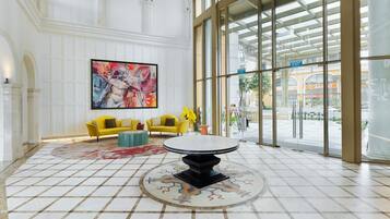 A lobby with a large window, a yellow sofa, a round table, and a large painting on the wall.