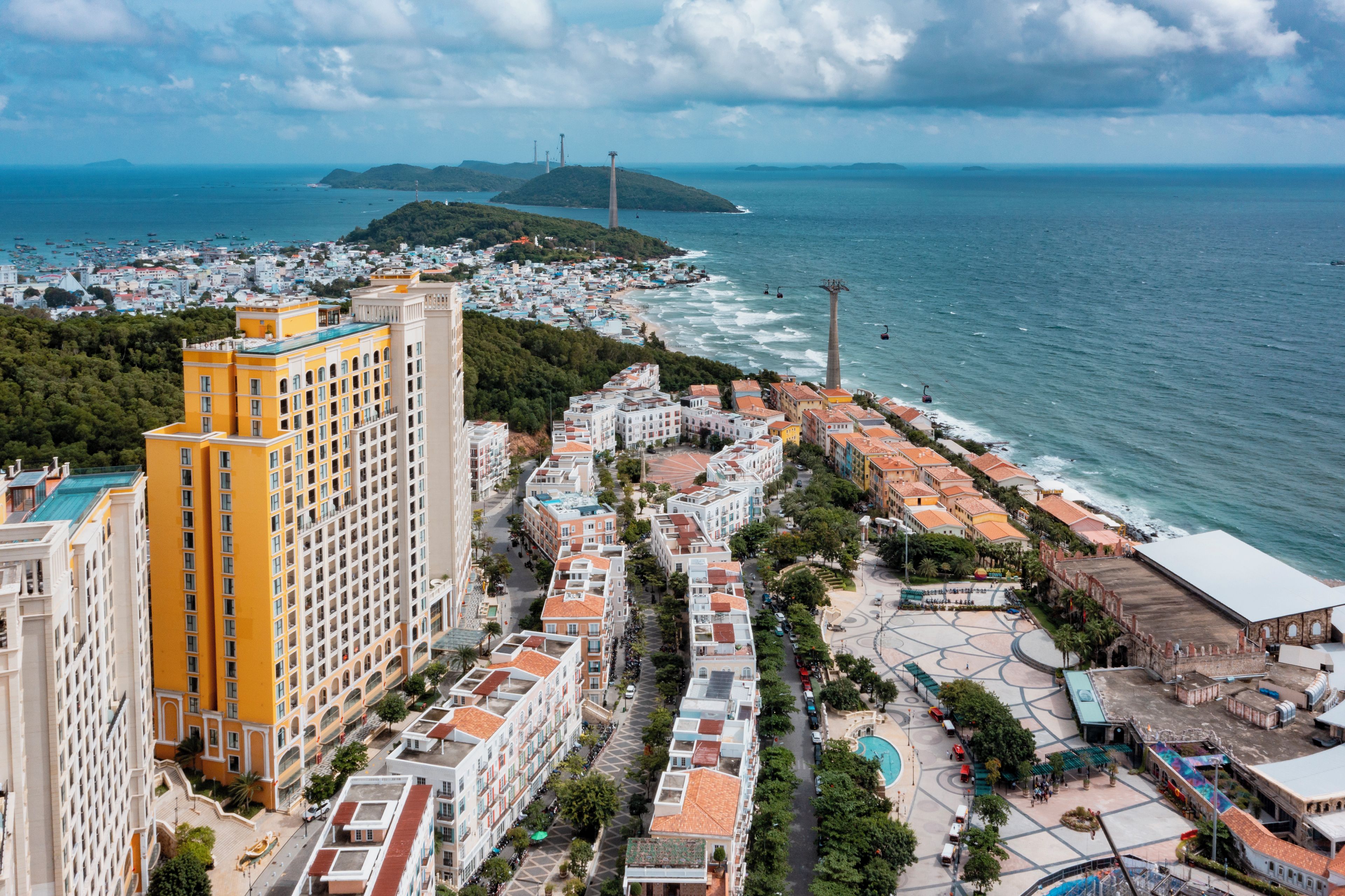 A coastal cityscape with a prominent yellow building, a marina, and a view of the sea.
