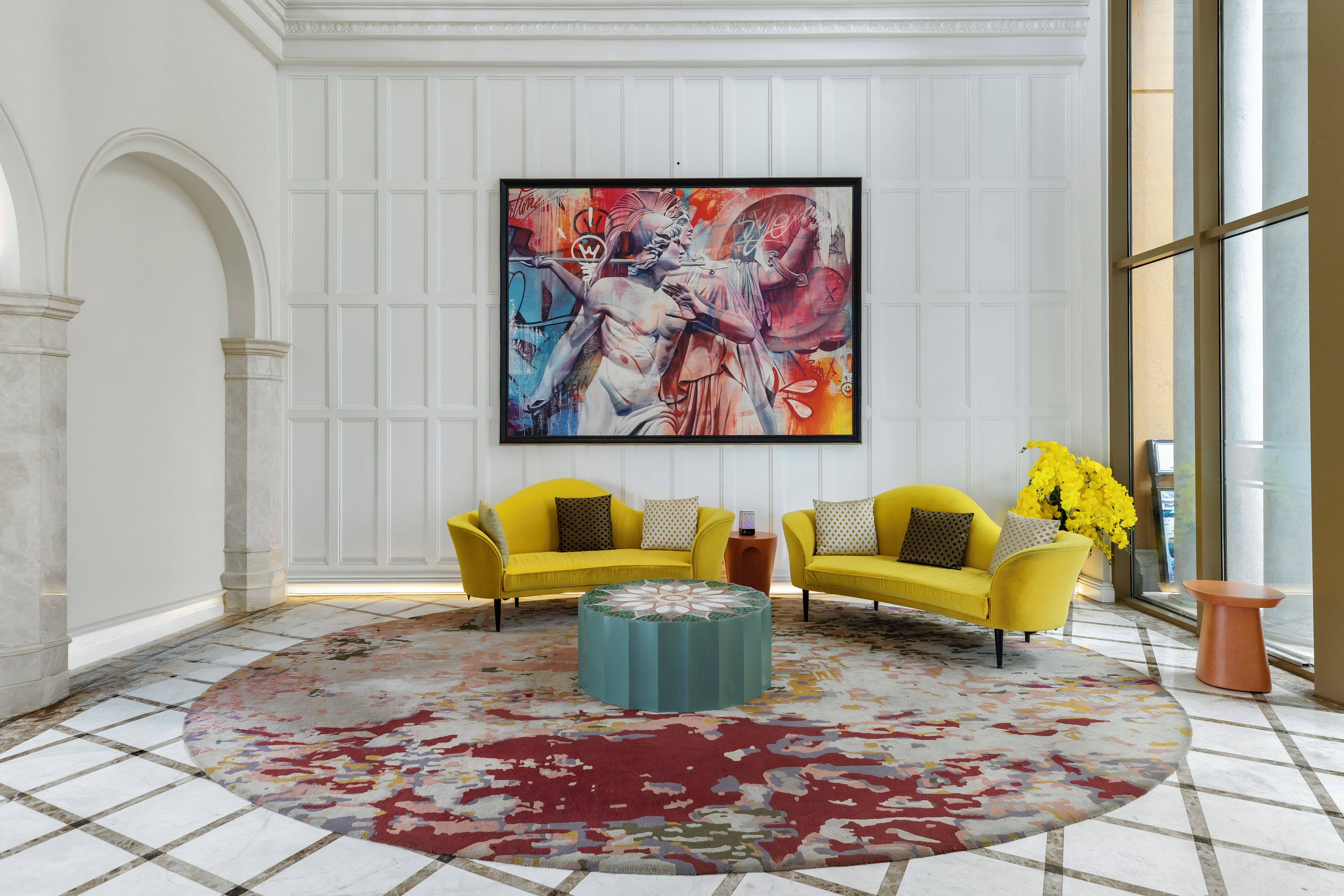 A room with two yellow sofas, a large abstract painting, and a patterned rug.