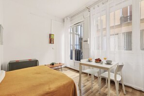 A room with a bed, a table with chairs, a radiator, and a window with a view of buildings. - Cute & Cozy Studio in Paris 11th (Paris)