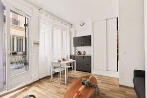 A compact living space with a dining area, kitchenette, and a sliding door leading to a balcony. - Cute & Cozy Studio in Paris 11th (Paris)