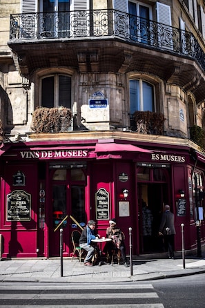 A red building with a sign reading "VINS DE MUSEES" and "ES MUSEES" indicating a wine shop and museum. - Cute & Cozy Studio in Paris 11th (Paris)
