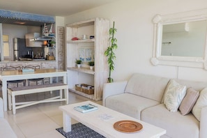 Een woonkamer met een witte bank, een salontafel, en een eethoek met een witte tafel en stoelen.